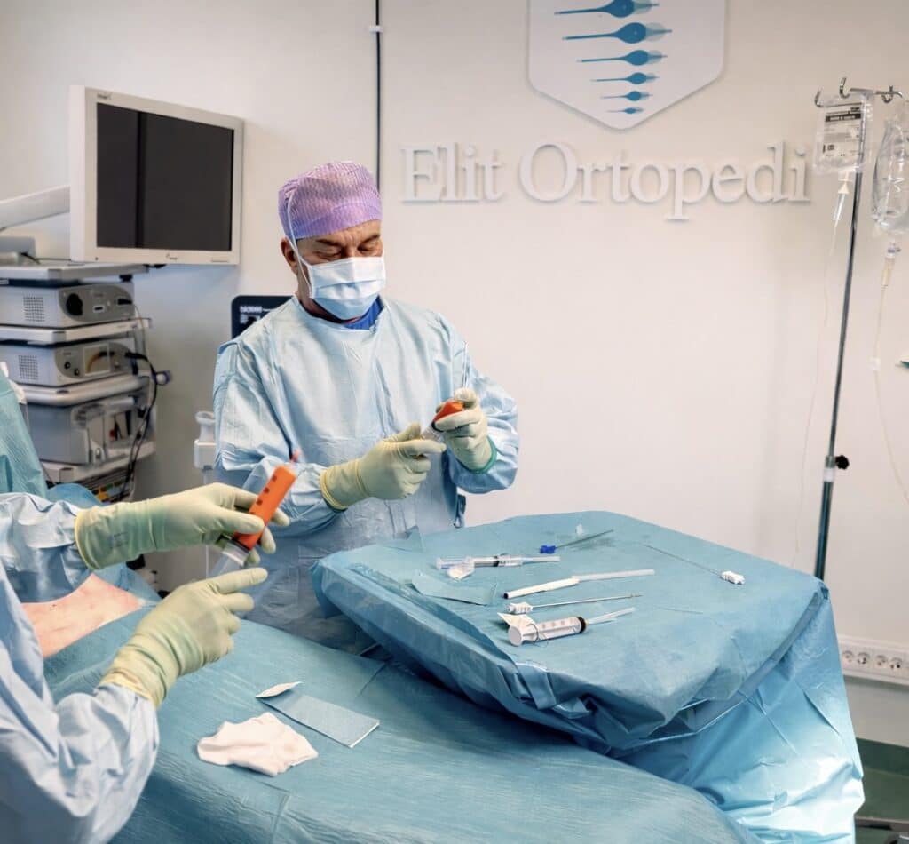Orthopedic specialist in blue surgical scrubs harvesting and preparing stem cells for regenerative joint treatment in a modern operating room at Elit Ortopedi, Stockholm.